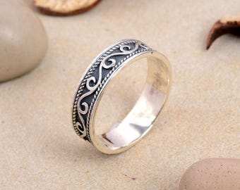 May include: A silver ring featuring a detailed, dark-toned, swirling pattern encircling the band. The ring is displayed against a neutral backdrop, emphasising its intricate design and polished finish. The ring's design is symmetrical and elegant.