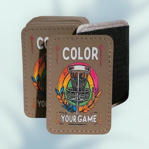 Könnte beinhalten: Ein Satz brauner Leder-Discgolf-Scorecard mit einem bunten Discgolf-Korbdesign und dem Text "COLOR YOUR GAME".