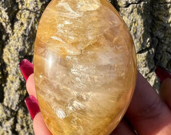 May include: A large, smooth, golden citrine crystal with a polished finish. The crystal has a translucent appearance with visible internal striations.
