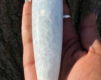 May include: A white, smooth, polished selenite crystal wand with a pointed tip. The crystal has a unique, textured surface with a slight iridescent sheen.