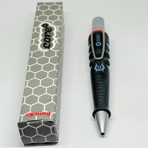 Op de afbeelding: Een zwarte en zilveren mechanische potlood met een bijpassende zeshoekige patroon doos. De potlood heeft een getextureerde grip, een zilveren punt en een metalen clip. De doos heeft de woorden "core" en "rotring" erop.
