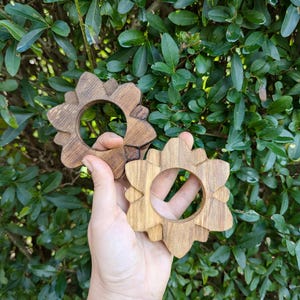 May include: Two wooden napkin rings in the shape of a flower. The rings are made of light brown wood and have a natural finish.