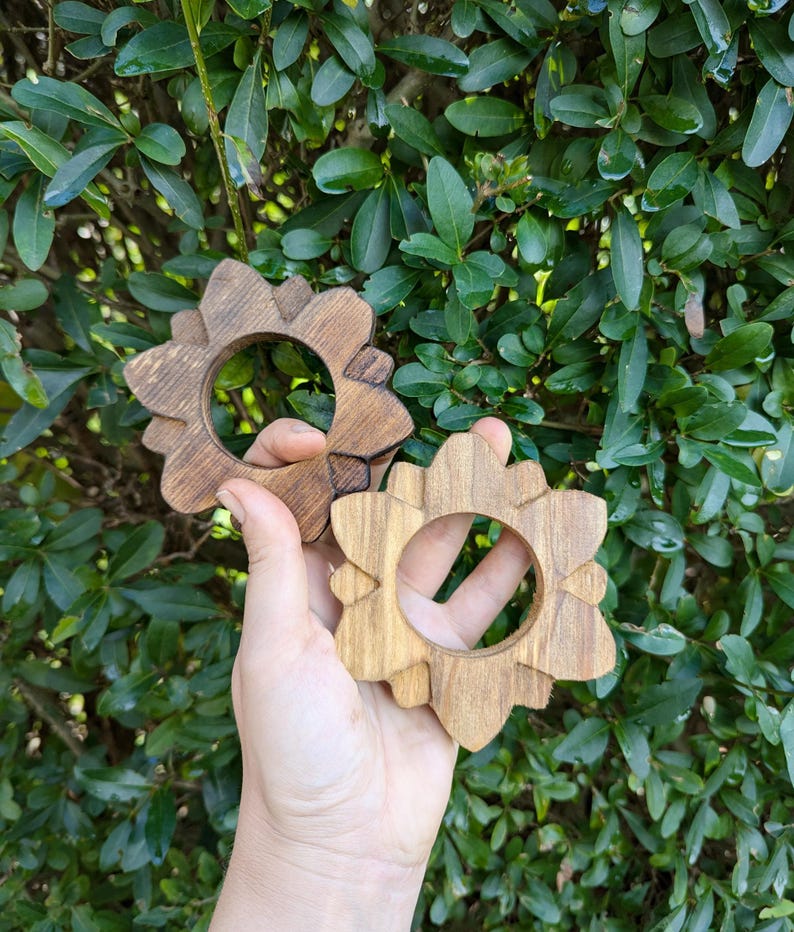 May include: Two wooden napkin rings in the shape of a flower. The rings are made of light brown wood and have a natural finish.