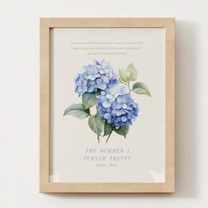 Puede incluir: Impresión enmarcada con una ilustración de acuarela de hortensias azules y hojas verdes. La obra de arte incluye texto de "El verano en que me enamoré" de Jenny Han. El marco es de madera clara.