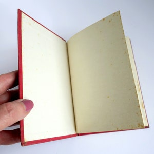 May include: A red hardcover book with blank pages is open to reveal the inside. The pages are slightly yellowed with age.