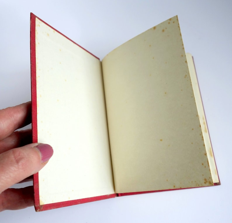 May include: A red hardcover book with blank pages is open to reveal the inside. The pages are slightly yellowed with age.