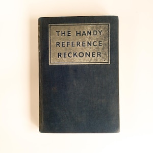 Peut inclure: Un livre relié de couleur bleue avec le titre "The Handy Reference Reckoner" imprimé en lettres dorées sur la couverture.