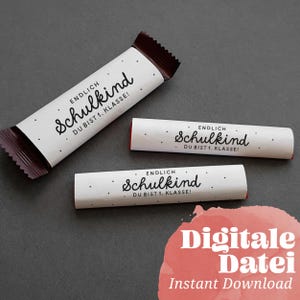 Puede incluir: Tres envoltorios blancos de barritas de caramelo con el texto "ENDLICH Schulkind DU BIST 1. KLASSE!" en escritura negra y pequeños puntos negros. Un envoltorio está abierto, revelando un interior marrón. Las palabras "Digitale Datei Instant Download" están en un círculo rosa.