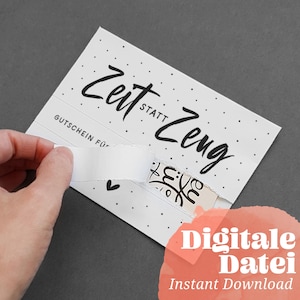 Puede incluir: Una tarjeta blanca con texto negro que dice "Zeit statt Zeug" y "Gutschein für". La tarjeta tiene un pequeño corazón blanco en la esquina inferior izquierda. Una mano está despegando una pestaña de papel blanco para revelar un diseño en blanco y negro.