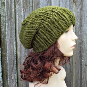 May include: A green knitted beanie hat with a slouchy fit. The hat is made with a thick yarn and has a simple, ribbed design.