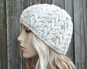 May include: A white knitted beanie with a chevron pattern. The beanie is made of a soft, fluffy yarn.