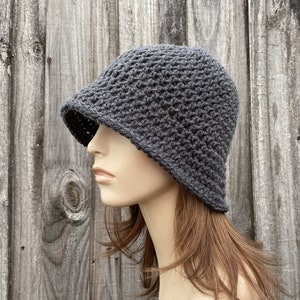 May include: A gray crocheted bucket hat with a textured stitch pattern. The hat is worn on a mannequin with brown hair.