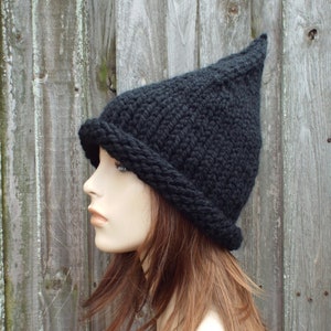 Könnte beinhalten: Eine schwarze Strickmütze mit spitzer Spitze und dickem, umgeschlagenem Rand. Die Mütze ist aus dickem Garn gefertigt und hat ein strukturiertes Aussehen. Die Mütze wird auf einem Schaufensterkopf gezeigt.