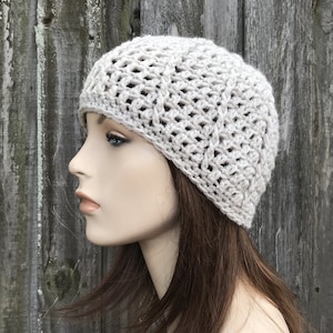 May include: A beige crocheted beanie hat with a textured pattern. The hat is worn on a mannequin head with long brown hair.