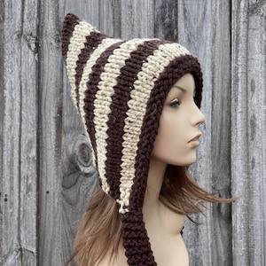 May include: A brown and cream striped knit hat with a long pointed hood and matching ties. The hat is made of a soft, warm yarn and is perfect for keeping your head and ears warm in the winter.