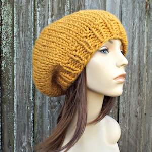 May include: A mustard yellow knitted beanie hat with a slouchy fit. The hat is made of a soft, chunky yarn and has a simple, classic design.