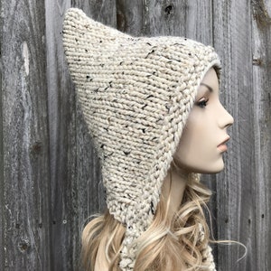 May include: A white knitted hooded hat with a long pointed tip and a thick, textured yarn. The hat is shown on a mannequin with long blonde hair.