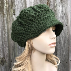 Könnte beinhalten: Eine dunkelgrüne, gehäkelte Newsboy-Mütze mit breitem Schirm. Die Mütze ist mit einem strukturierten Stichmuster gearbeitet.