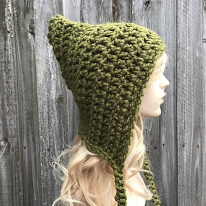 May include: A green crocheted hat with a long pointed crown and two long ties. The hat is worn on a mannequin with long blonde hair.
