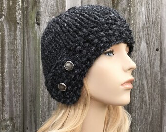 May include: A black knitted cloche hat with a slouchy fit and two silver buttons on the side.