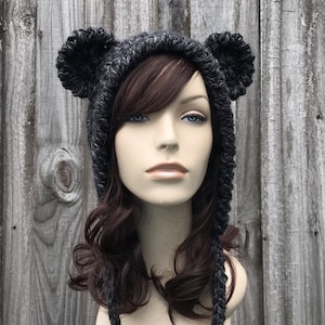 May include: A gray hooded hat with bear ears. The hat is knitted and has a long, braided tie.