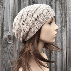 May include: A beige knitted beanie with a ribbed texture. The beanie is on a mannequin head with long brown hair.