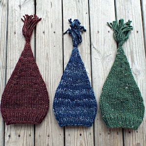 Può includere: Tre cappelli di lana con nappe in bordeaux, blu e verde.