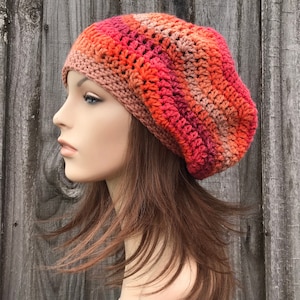 Puede incluir: Un gorro de punto en tonos naranja, rojo y marrón. El gorro es holgado y tiene un ala ancha.