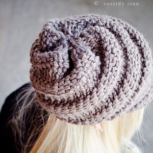 Könnte beinhalten: Nahaufnahme einer Frau, die eine graue Strickmütze trägt. Die Mütze hat ein strukturiertes, Zopfmuster. Die Frau hat langes, blondes Haar.