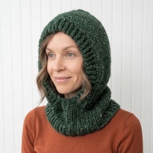 May include: A dark forest green chunky knit balaclava hood with a ribbed texture and subtle white flecks throughout the yarn. The head covering features a thick, wide ribbed border around the face opening and a snug fit around the neck area.