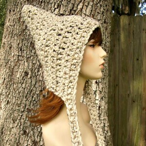 May include: A beige crocheted hooded hat with long ties. The hat is made with a textured yarn and has a pointed hood.