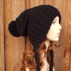 Può includere: Berretto di lana nero con un pon pon in cima e lunghe trecce che pendono dalla schiena. Il berretto è su una testa di manichino con lunghi capelli rossi ricci.