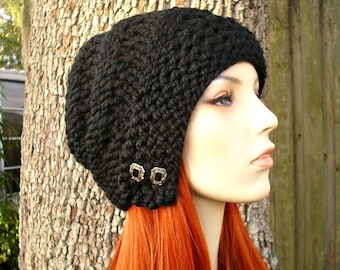 May include: A black knitted beanie with two gold buttons. The beanie is slouchy and has a wide brim.