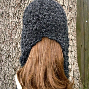 May include: A gray crocheted hat with a long, flowing design. The hat is worn on a person with long brown hair.