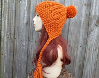 May include: A bright orange knitted hat with a long tassel and a pom-pom on top. The hat is worn on a mannequin with long red hair.