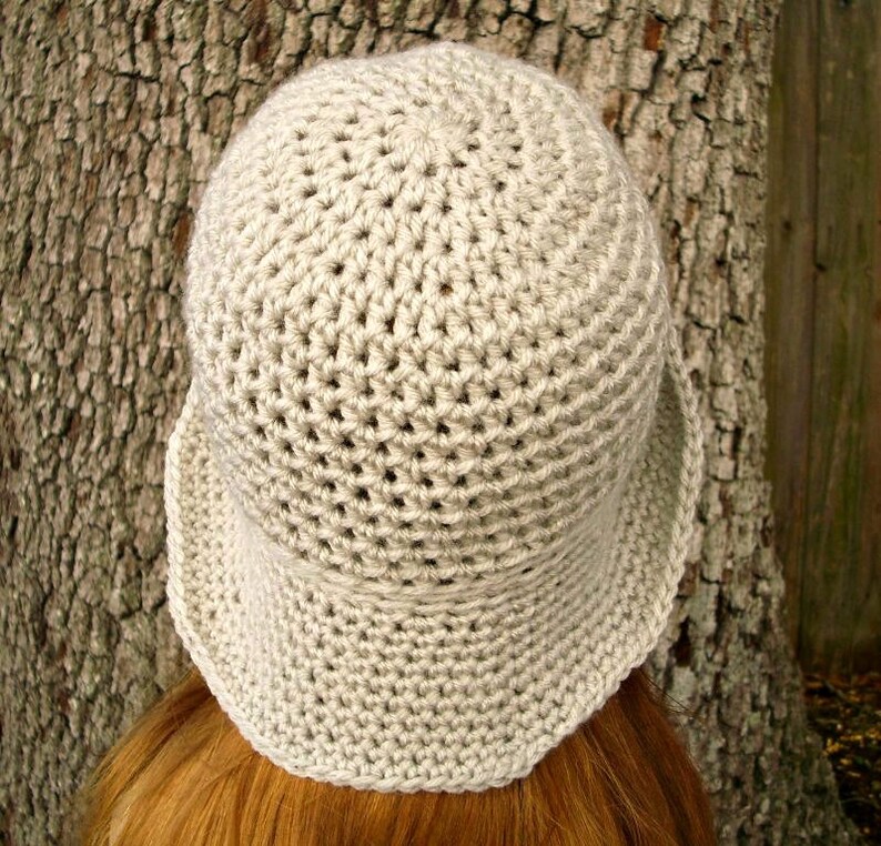 May include: A crocheted hat in a light beige color. The hat has a wide brim and a rounded crown.