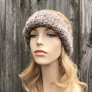 May include: A knitted beanie hat in a light brown color with a subtle pattern of beige and mustard yellow stripes. The hat is made of soft yarn and has a slouchy fit.