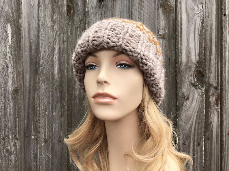 May include: A knitted beanie hat in a light brown color with a subtle pattern of beige and mustard yellow stripes. The hat is made of soft yarn and has a slouchy fit.