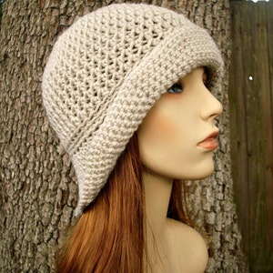 May include: A beige crocheted cloche hat with a wide brim. The hat is made with a simple stitch pattern and has a soft, slouchy fit.