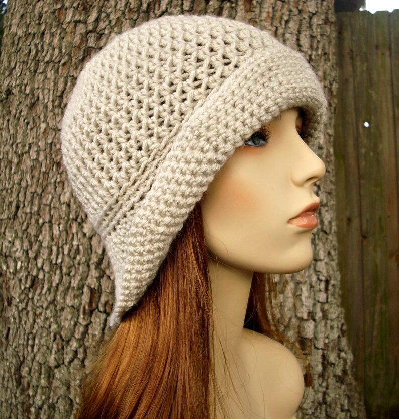 May include: A beige crocheted cloche hat with a wide brim. The hat is made with a simple stitch pattern and has a soft, slouchy fit.