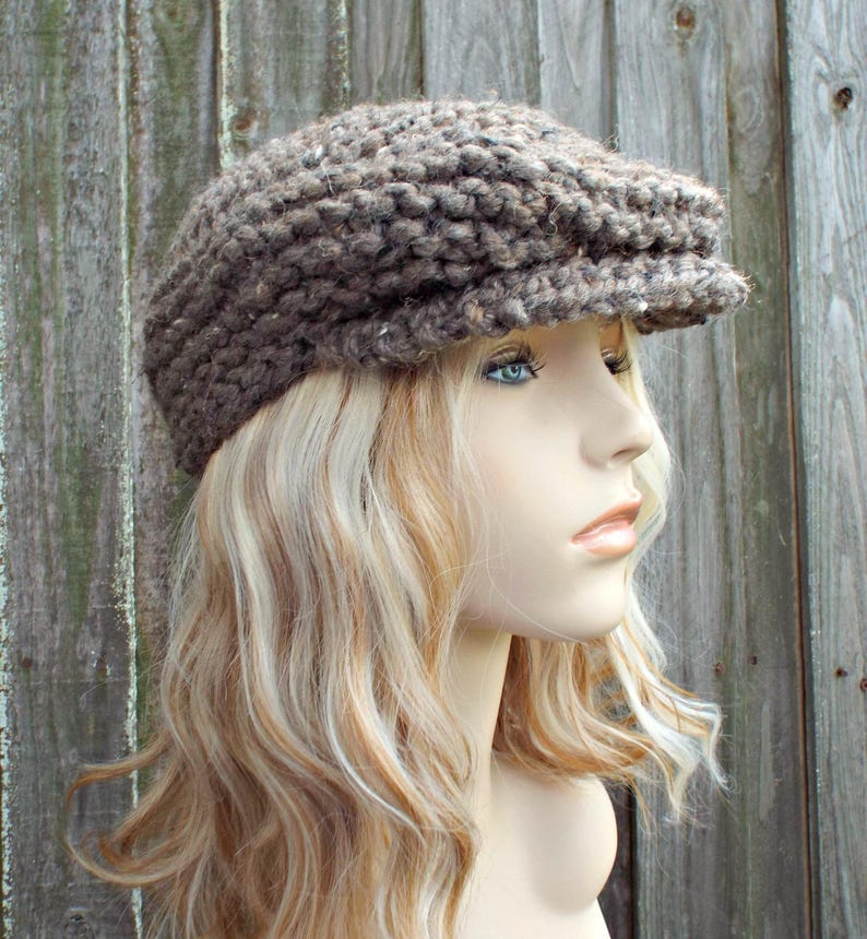 May include: A brown, chunky knit newsboy cap featuring a textured, thick yarn construction with subtle flecks of lighter color throughout. The hat has a rounded crown and a short, stiffened brim extending from the front, crafted in a rustic style.