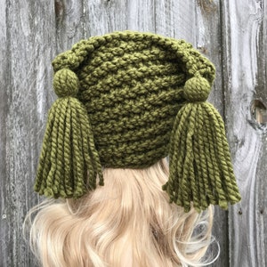 May include: A green knitted hat with two long tassels. The hat is made with a chunky yarn and has a simple, classic design.