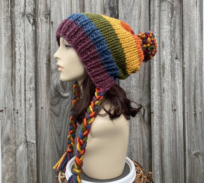 Pu&ograve; includere: Un cappello di lana colorato con un pon pon in cima e lunghi lacci intrecciati. Il cappello &egrave; realizzato in un motivo arcobaleno di rosso, arancione, giallo, verde, blu e viola.