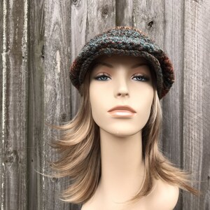 Op de afbeelding: Een bruine, groene en oranje getweedde newsboy-pet met een platte klep.