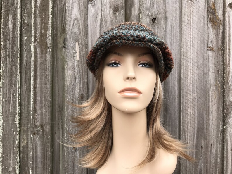 Op de afbeelding: Een bruine, groene en oranje getweedde newsboy-pet met een platte klep.