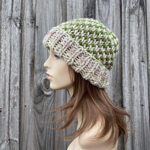 May include: A knitted beanie hat with a green and pink color pattern. The hat is made with a chunky yarn and has a slouchy fit.