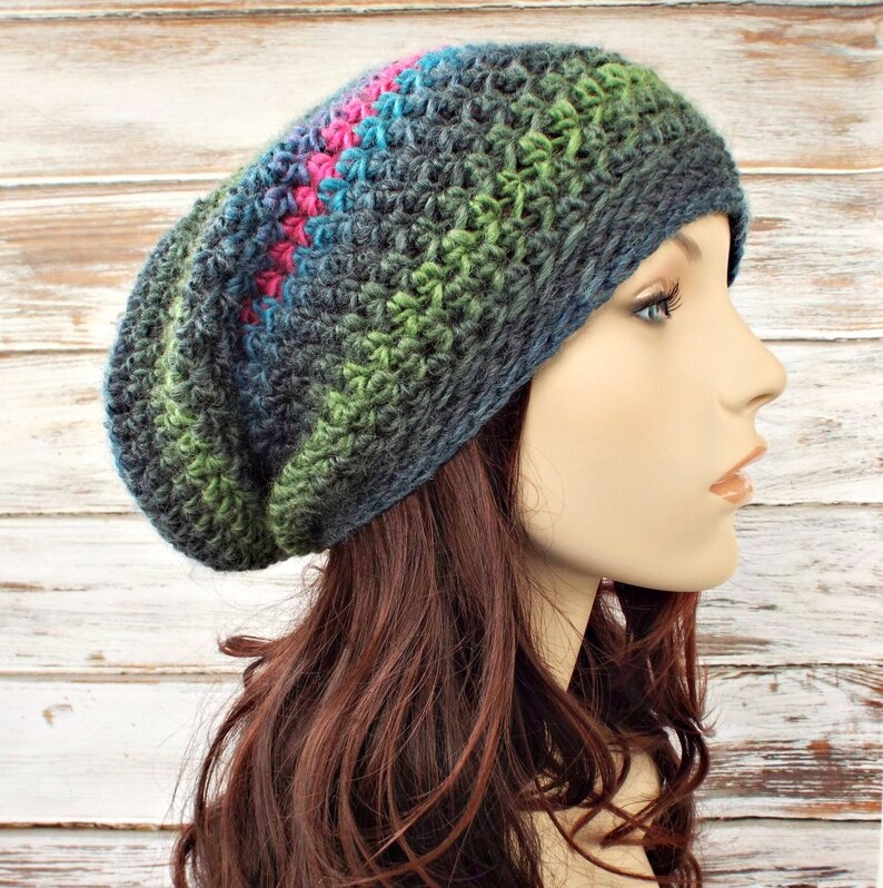 Puede incluir: Un gorro de punto slouchy en un degradado de colores azul oscuro, verde y rosa. El gorro est&aacute; tejido a crochet con un punto texturizado.