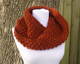 May include: A warm, rust-colored knitted cowl neck scarf. The scarf is made of a soft, chunky yarn and is perfect for keeping warm in the winter.