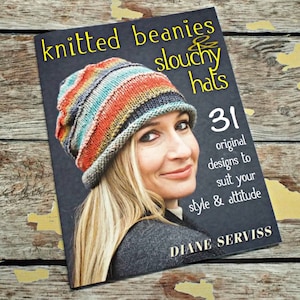 May include: Book cover featuring a woman wearing a colorful knitted beanie. The title is "Knitted Beanies & Slouchy Hats" with the subtitle "31 original designs to suit your style & attitude". The author is Diane Serviss.