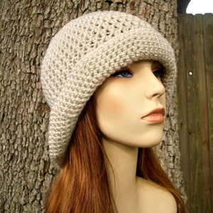 May include: A beige crocheted cloche hat with a wide brim. The hat is worn by a mannequin with long, red hair.